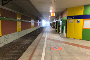 Ein Bahnhofsgebäude in Berlin, Deutschland, mit einem Zug auf den Schienen, beleuchtet von Deckenlampen, Graffiti an der linken Wand und einigen Gegenst√§nden auf der rechten Seite.