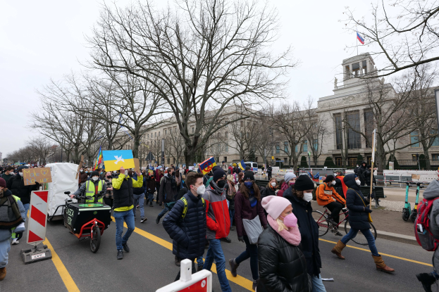 Eine große Gruppe von Menschen bei einer Protestdemo in Washington, D.C. am 21. Januar 2020, die eine Straße mit Plakaten, Schildern und Fahrrädern entlanggehen, vor einer Gebäudefassade, Bäumen und einem klaren blauen Himmel.