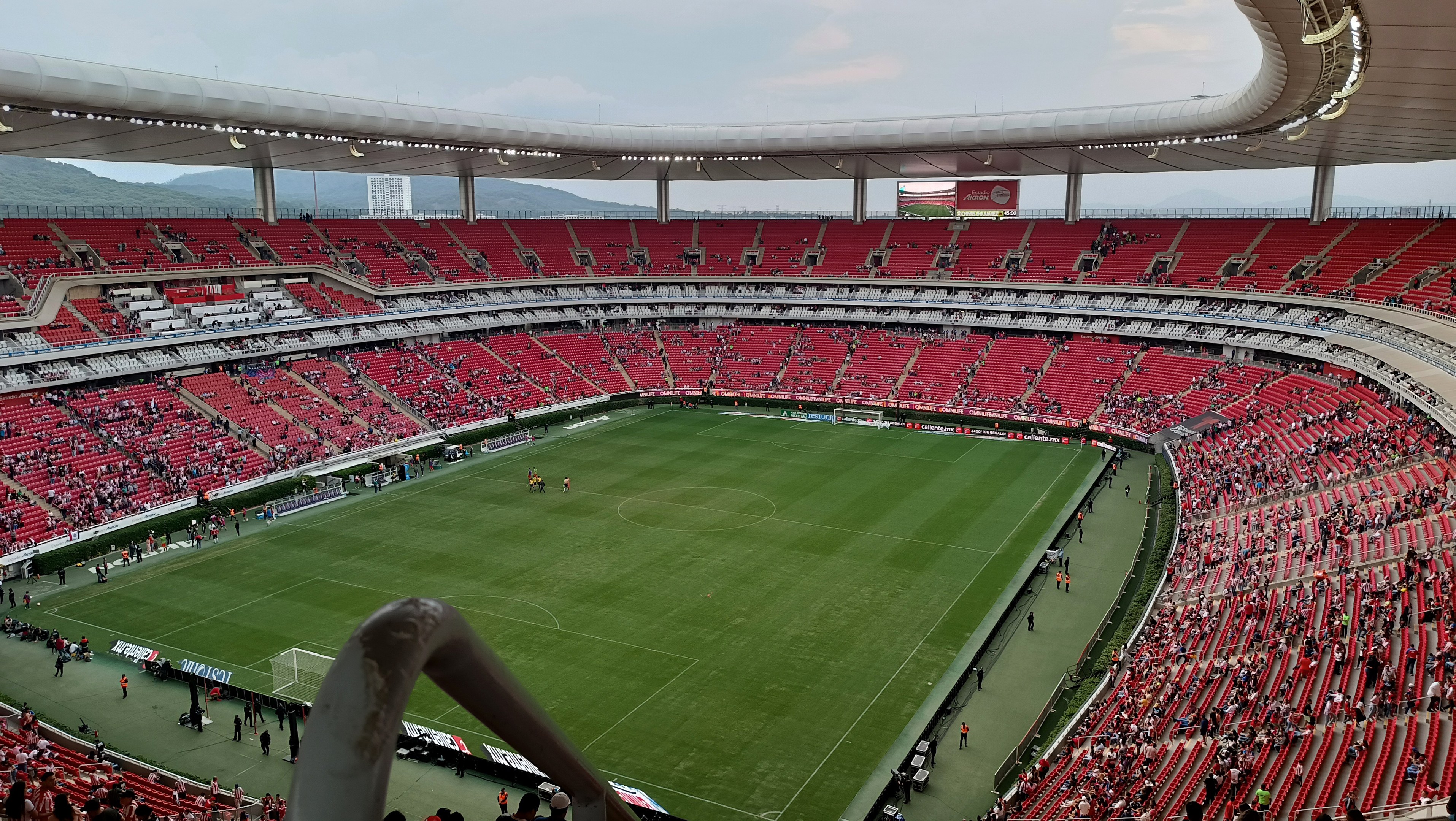 Großes Stadion voller Zuschauer bei einem Fußballspiel, Hügel im Hintergrund bei klarem blauem Himmel.