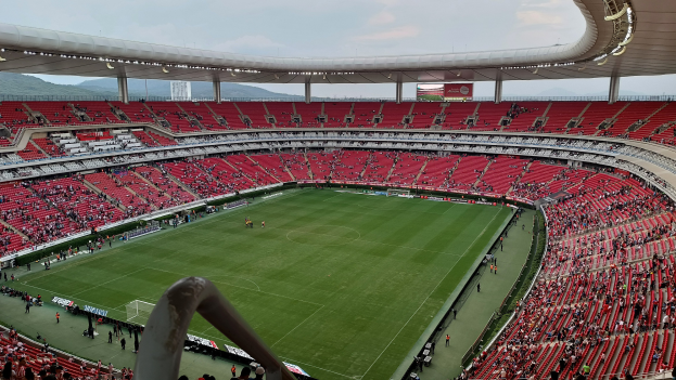 Großes Stadion voller Zuschauer bei einem Fußballspiel, Hügel im Hintergrund bei klarem blauem Himmel.