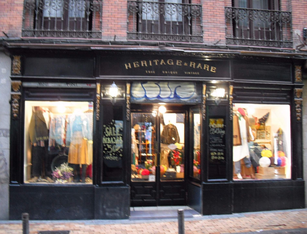 Heritage Boutique in Madrid mit Schaufensterpuppen, die Kleider tragen, Fenstern, Geländern, einem Namensschild und Straßenbeleuchtung.