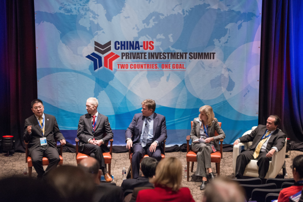 Eine Gruppe von Menschen, die auf Stühlen sitzen und auf einen Bildschirm mit Text und einer Karte schauen, mit Vorhängen im Hintergrund, was auf einen China-US-Privatinvestment-Gipfel hindeutet.