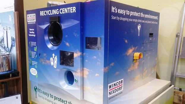 Blauer Recyclinghof mit einem "Recyclinghof"-Schild in der Mitte, einem Gestell mit Gegenständen links, einem Gegenstand auf dem Boden rechts und Lichtern und einer Wand im Hintergrund.