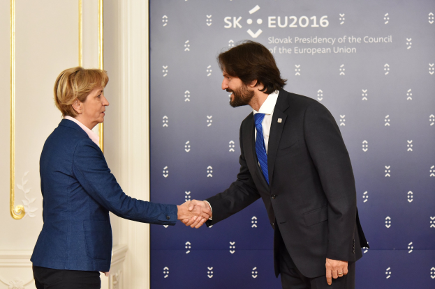Bundeskanzlerin Angela Merkel und Bundespräsident Joachim Gauck schütteln Hände vor einer Wand mit einem "EU-Gipfel"-Schild und einer Tür im Hintergrund, beide lächeln.