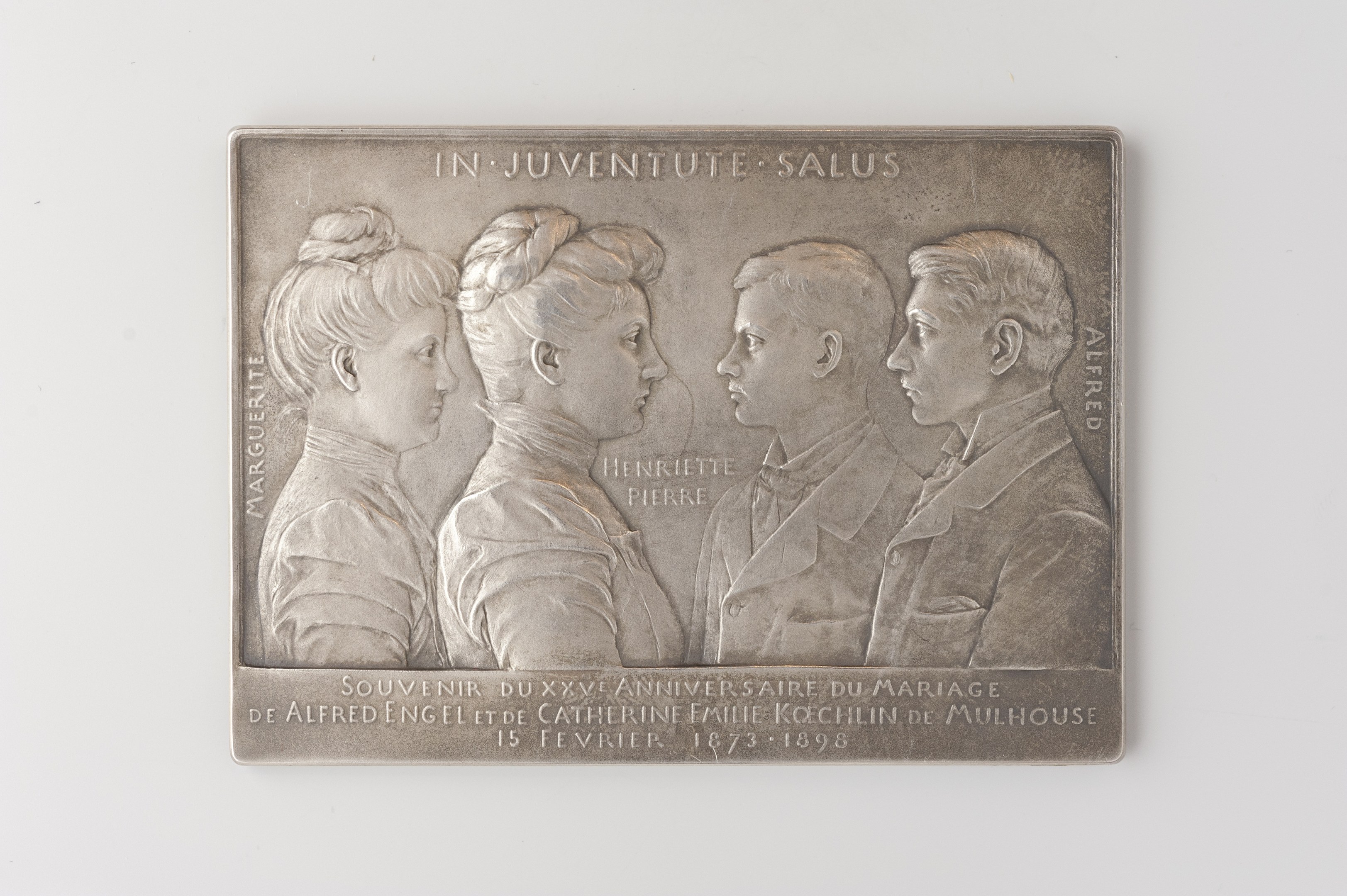 Silberne Plakette mit einem eingravierten Bild von drei Menschen und Text auf einem weißen Hintergrund, wahrscheinlich zur Erinnerung an eine Hochzeit.