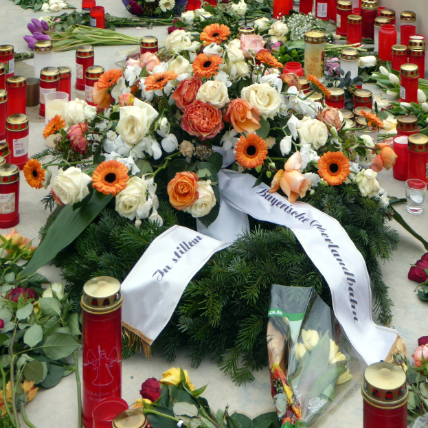 Mahnmal in Berlin mit Blumen und Kerzen vor einer Wand auf dem Boden plaziert.
