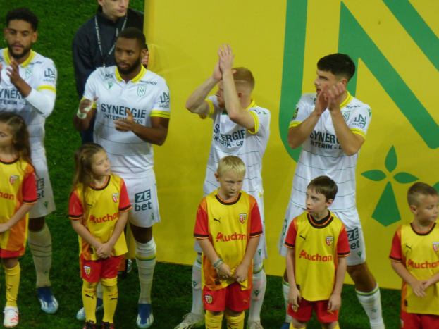 Junge Fußballer in Uniformen klatschen in Feierlaune auf einem Ligue 1-Feld, mit einem "Ligue 1"-Schild im Hintergrund.