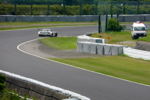 Eine Person fährt ein rotes Auto mit hoher Geschwindigkeit auf einer Rennstrecke, mit einem Verkehrskegel vor sich und einem unscharfen Hintergrund.