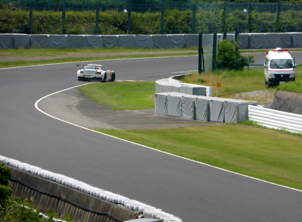 Eine Person fährt ein rotes Auto mit hoher Geschwindigkeit auf einer Rennstrecke, mit einem Verkehrskegel vor sich und einem unscharfen Hintergrund.