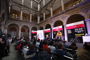 Eine Gruppe von Menschen, die an einem Tisch mit einem Podium und einem Mikrofon vor einer Menge, Kameras und Transparenten sitzt, während einer Pressekonferenz für das CDMX 2017-Event.