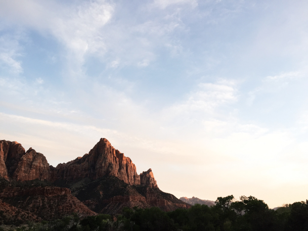 Ein atemberaubender Blick auf den Zion-Nationalpark in Utah mit Bäumen, Hügeln und einem Himmel voller Wolken, erhellt von der untergehenden Sonne.