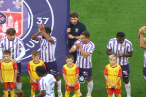 Eine Gruppe junger Jungs steht auf einem grünen Fußballfeld, klatscht in die Hände mit einem Banner und Logos im Hintergrund.