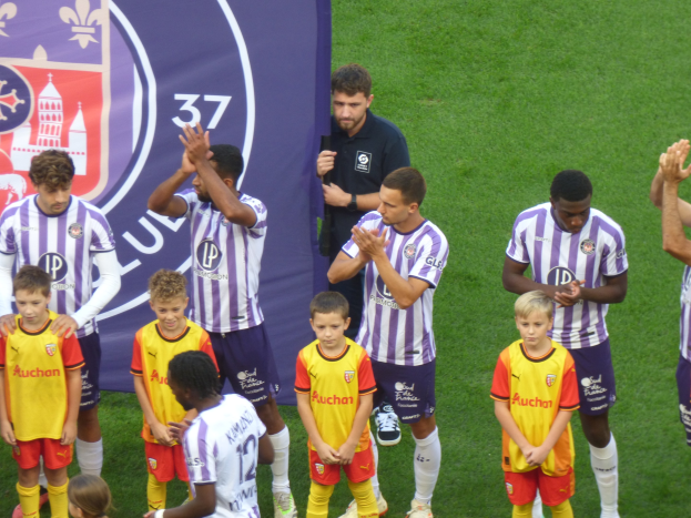 Eine Gruppe junger Jungs steht auf einem grünen Fußballfeld, klatscht in die Hände mit einem Banner und Logos im Hintergrund.