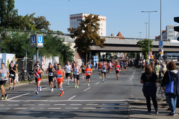 Gruppe von Menschen beim Laufen in einem Marathon auf einer von Bäumen gesäumten Straße unter einem klaren blauen Himmel.