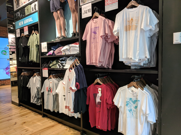 Eine Disney-Store-Ausstellung voller T-Shirts an Bügeln und Tafeln mit Text und Bildern von Menschen, mit einem Bildschirm links und dem Boden unten.