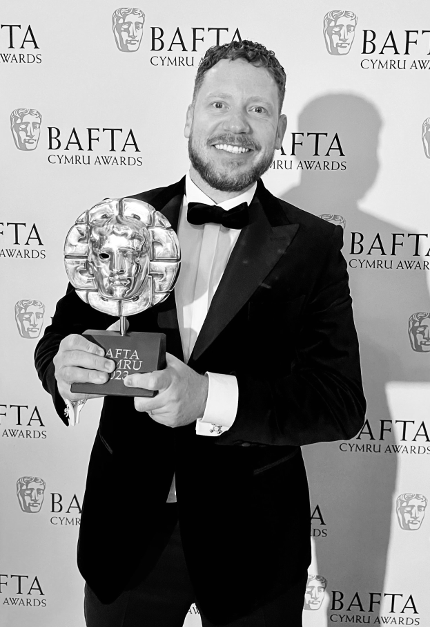 Ein Mann in einem Smoking, der eine BAFTA-Auszeichnung hält und lächelt, mit einem Hintergrund, auf dem 'BAFTA Awards 2018' steht
