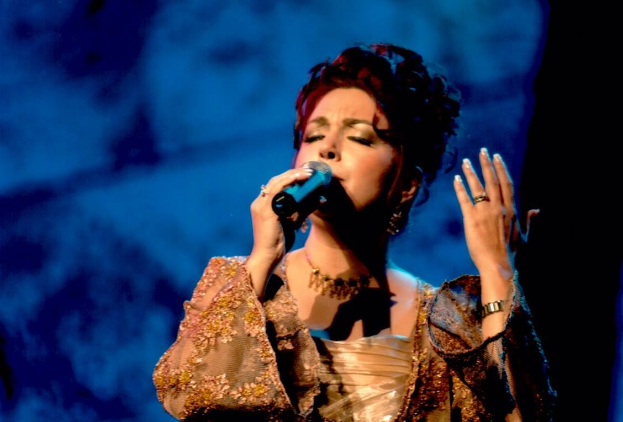 Eine Frau in einem goldenen Kleid, die auf der ESC-Bühne in ein Mikrofon singt.
