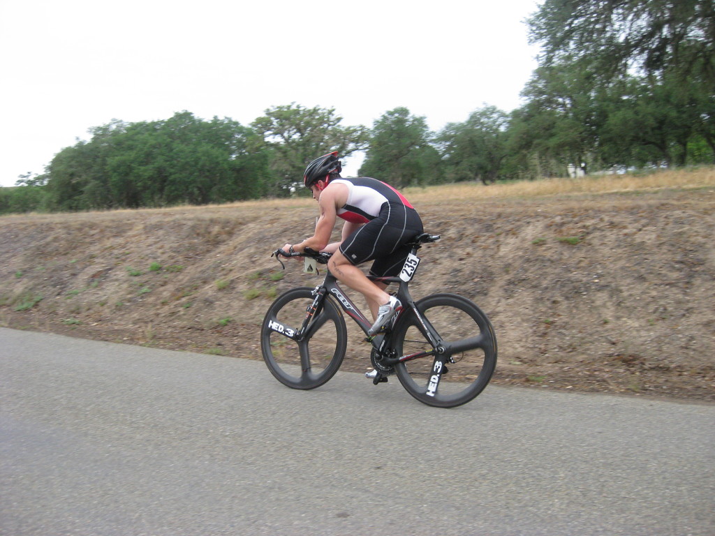 Eine Person mit Helm f√§hrt ein Fahrrad neben B√§umen und Gras.
