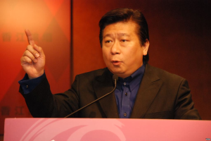 Ein Mann im Anzug und mit Krawatte hält eine Rede an einem Rednerpult mit Mikrofon und sieht ernst aus.