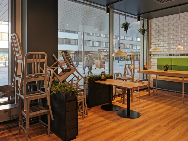 Restaurant-Innenraum mit hölzernen Tischen und Stühlen in der Nähe eines großen Fensters, das auf eine Berliner Straße mit Fußgängern, Gebäuden und städtischen Elementen blickt.