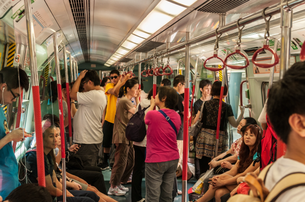 Menschen, die auf einem Zug fahren, einige sitzen und andere stehen, mit Metallstangen, Griffen und Deckenleuchten im Inneren.