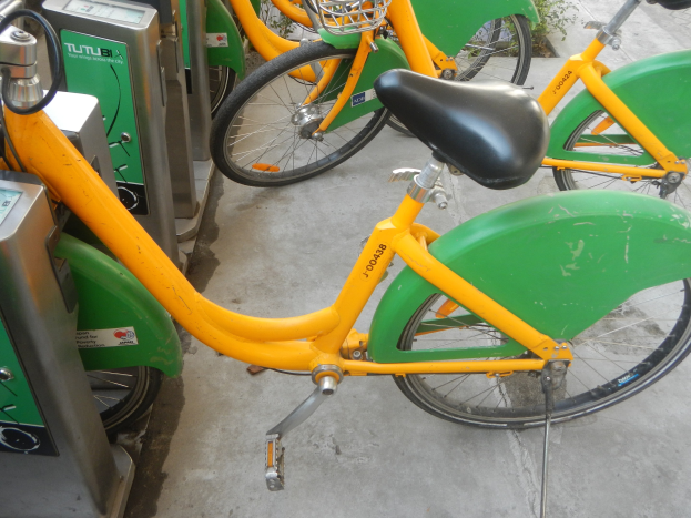 Eine Reihe gelber und grüner Fahrräder, die nebeneinander geparkt sind, mit Maschinen auf der linken Seite und Pflanzen im Hintergrund.