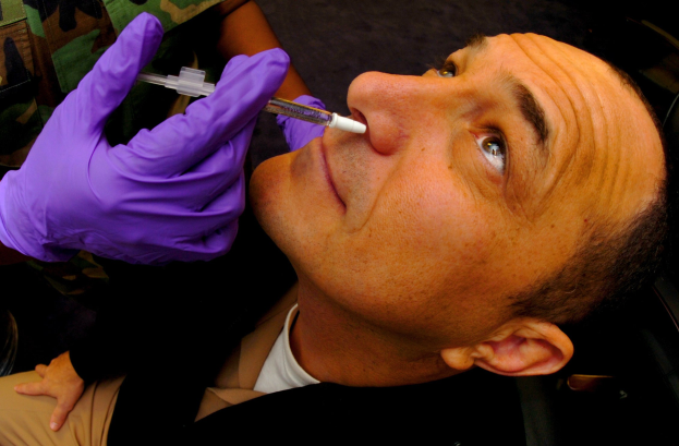 Ein Arzt in lila Handschuhen verimpft einem Mann ein Medikament mit einer Spritze in den Mund.