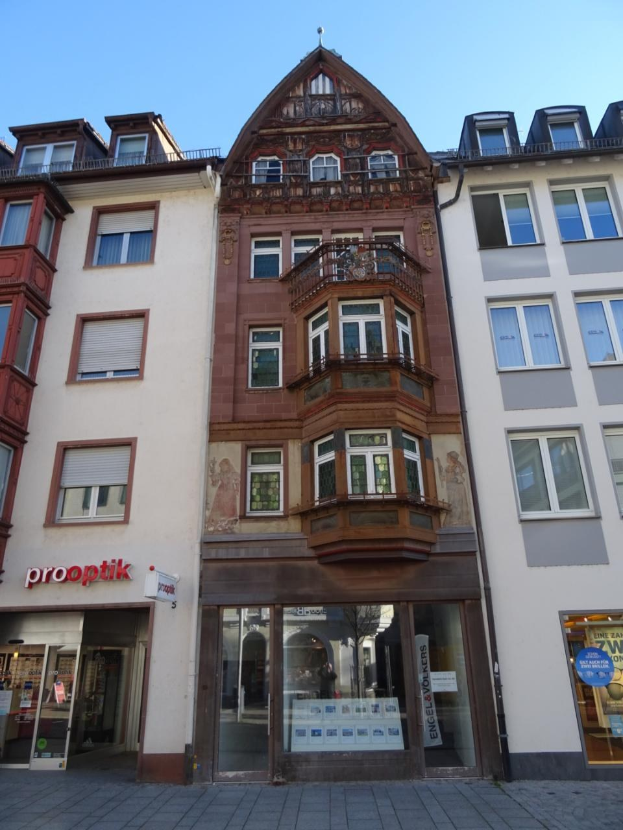 Ein kommerzielles Gebäude mit vielen Fenstern zum Verkauf, das sich auf einer Straße in Heidelberg, Deutschland, unter einem klaren blauen Himmel befindet.