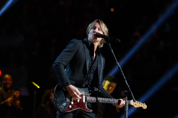 Keith Urban performs auf der Bühne im Joint in Las Vegas, spielt eine Gitarre mit einem Mikrofon davor und Musiker im Hintergrund, bei dunkler Beleuchtung.
