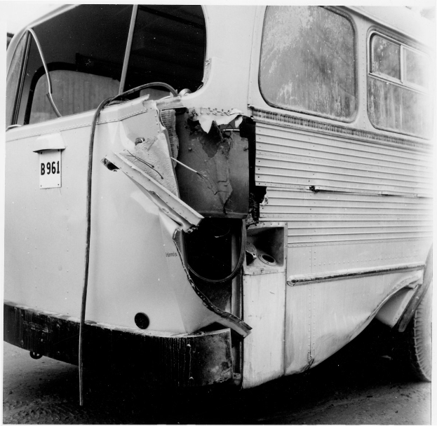 Schwarzes und weißes Foto eines Busses mit schwerer Frontalbeschädigung durch einen Autounfall auf der Straße.
