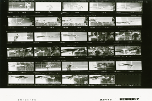 Ein Schwarz-Wei├č-Foto eines Mannes beim Tennisspielen, der ein wei├čes Hemd und Shorts tr├Ągt und einen Schl├Ąger in der rechten Hand h├Ąlt, mit einem konzentrierten Gesichtsausdruck und einem Filmstreifen im Hintergrund.