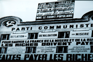 Ein Plakat an einer Gebäudeseite mit einem Hammer und Sichelsymbol, mit Text, der wahrscheinlich mit der Kommunistischen Partei in Verbindung steht.