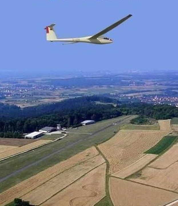 Ein Segelflugzeug fliegt über ein Feld mit Bäumen und Gebäuden im Hintergrund, mit Text oben auf dem Bild.