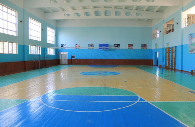 Großes Turnhalle mit blau-weißem Boden, Basketballfeld, Netz, Stangen, Tür, Fenstern, Wandplakaten, Geländer und Dach.