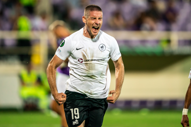 Ein Mann in weißem T-Shirt und schwarzen Shorts läuft auf einem Fuballfeld, feiert ein Tor, umgeben von einer Gruppe von Menschen, mit der Überschrift "Leeds United vs Melbourne Victory".