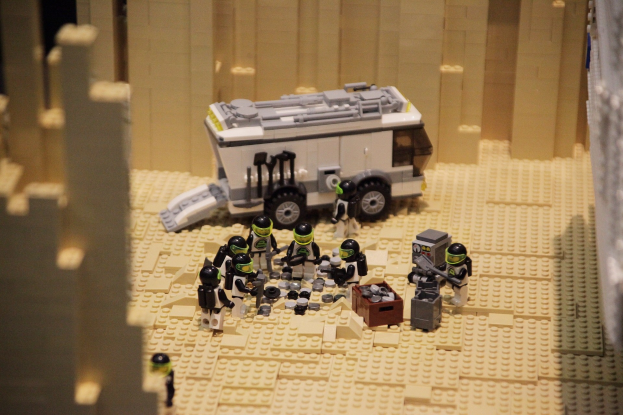 Lego-Modell einer Star-Wars-Szene mit einem Bodenfahrzeug im Vordergrund und einer Wand im Hintergrund sowie einigen verstreuten Spielzeugfiguren.