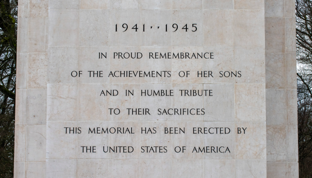 Ein Denkmal mit einer Tafel, auf der 'In stolzem Gedenken an die Leistungen ihrer Söhne und in Demut zu ihrem Opfer' eingraviert ist, vor einem Hintergrund aus Bäumen und einem klaren blauen Himmel.