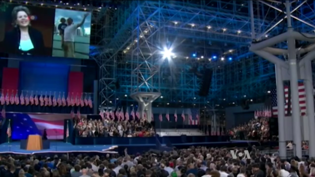 Eine große Menschenmenge sitzt vor einer Bühne mit einem Podium, einem Mikrofon, Flaggen, einem Bildschirm und Lichtausrüstung und wartet auf eine Präsidentschaftsdebatte.