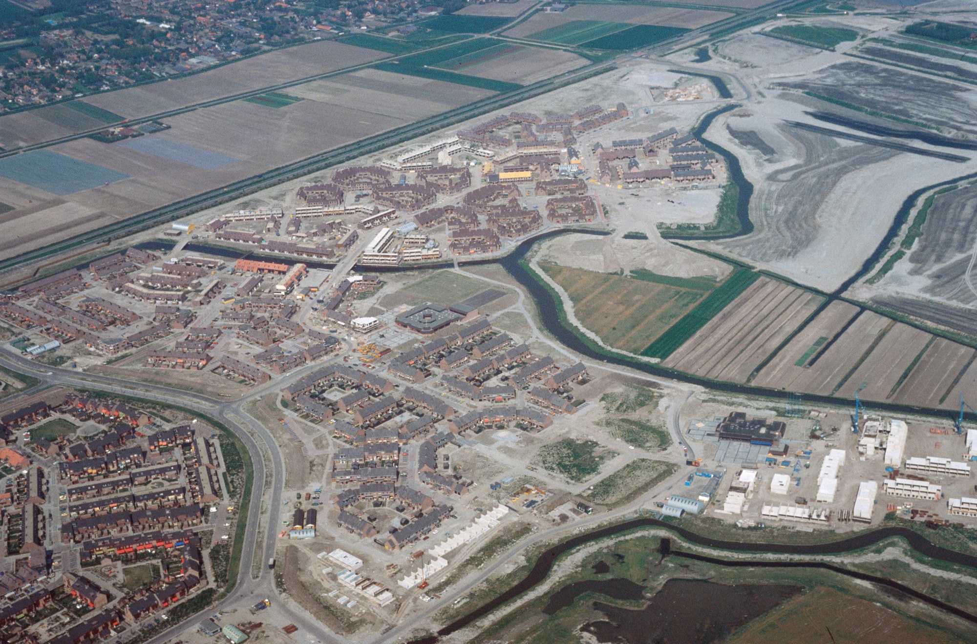 Luftaufnahme einer Stadt mit dichtem Baumbestand, Straßen, Feldern, Bäumen und einem zentralen Reservoir, das von städtischen Gebieten umgeben ist.