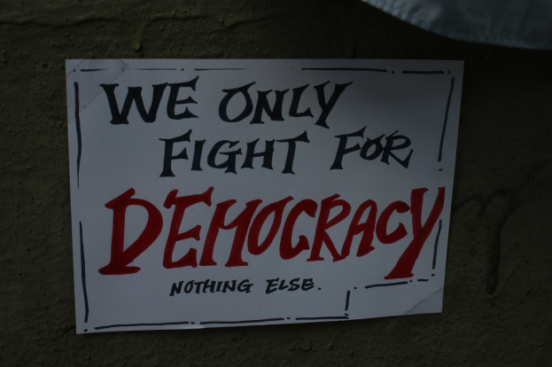Weißer Bericht mit den Worten "Wir kämpfen nur für Demokratie" an einer Wand angebracht.