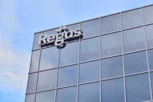 Ein Gebäude mit einer Regus-Tafel und dem Text "Regus investiert 1,5 Milliarden US-Dollar in US-Hauptstadt" unter einem bewölkten Himmel.