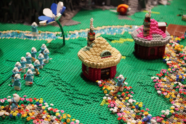 Ein Lego-Modell einer Kleinstadt mit bunten Blumen, Häusern, Pflanzen und verschiedenen Spielzeugen vor einem leicht unscharfen Hintergrund.