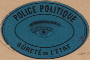 Ein brauner Karton mit einem blauen Aufkleber, auf dem "Polizei Politique Surete de L'Etat" steht und ein Auge in der Mitte zeigt.
