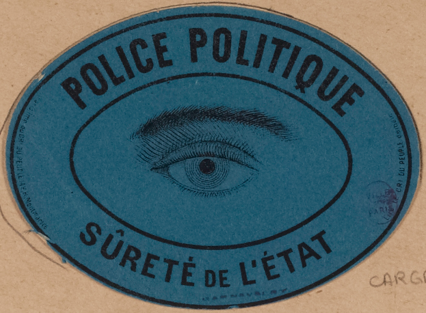 Ein brauner Karton mit einem blauen Aufkleber, auf dem "Polizei Politique Surete de L'Etat" steht und ein Auge in der Mitte zeigt.