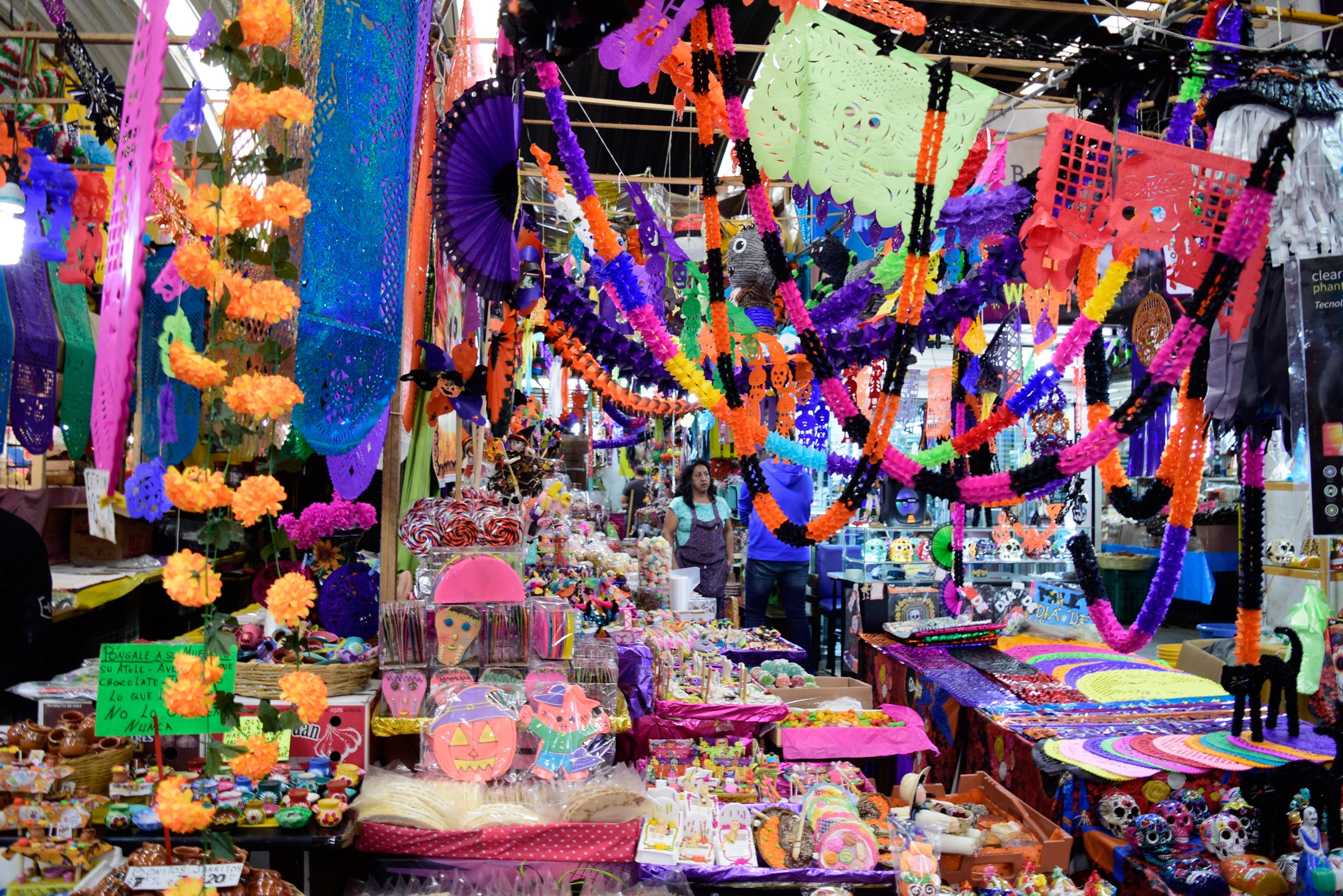 Ein belebter Markt mit verschiedenen zum Verkauf stehenden Gegenständen, darunter Spielzeuge und dekorative Gegenstände, unter einer mit Lichtern geschmückten Decke.