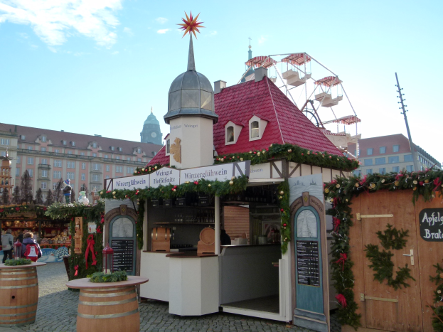 Ein kleines rotes Dachgebäude mit einem Riesenrad davor, umgeben von Menschen und Festdekorationen bei einem Oktoberfest-Event in München, Deutschland.