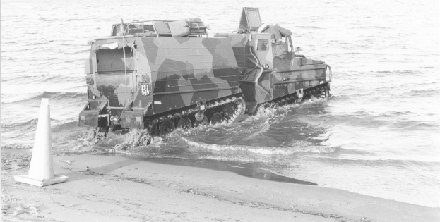 Schwarzes und weißes Foto eines Amphibienfahrzeugs, das durch Wasser fährt, mit einem Verkehrskegel links und Sand unten.