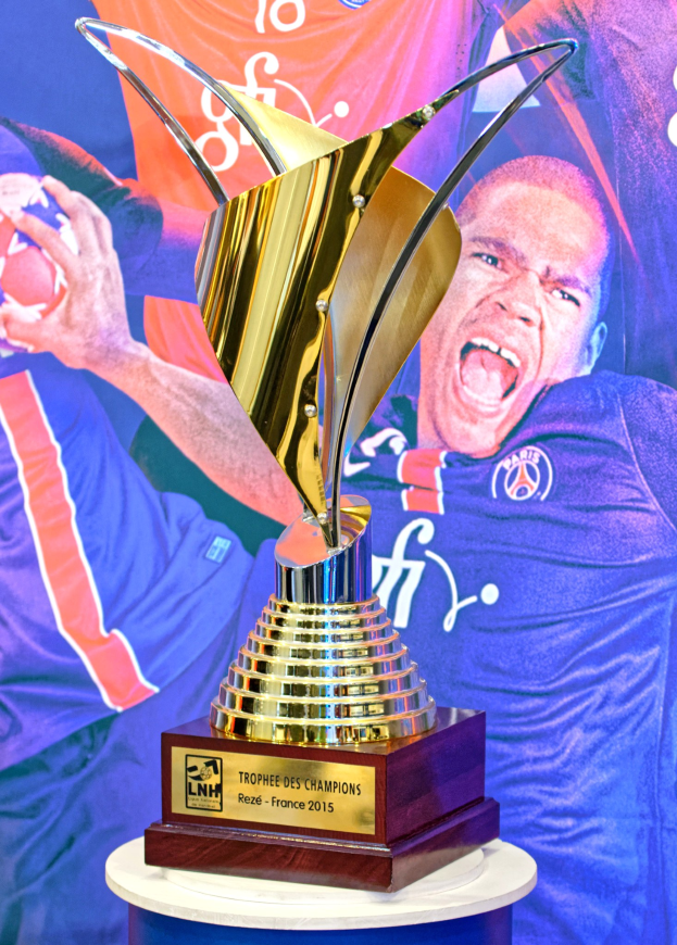 Ein silberger Pokal auf einem Tisch mit einem unscharfen Banner im Hintergrund, das ein Personenbild zeigt.