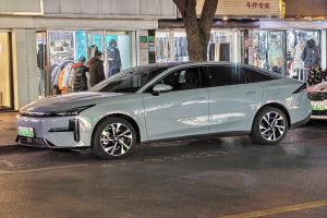 Ein Mitsubishi Lancer EV Elektroauto, das nachts auf einer Straße geparkt ist, umgeben von Gebäuden, Geschäften, Schaufensterpuppen mit Kleidern, Schildern mit Text, Lichtern und anderen Gegenständen.