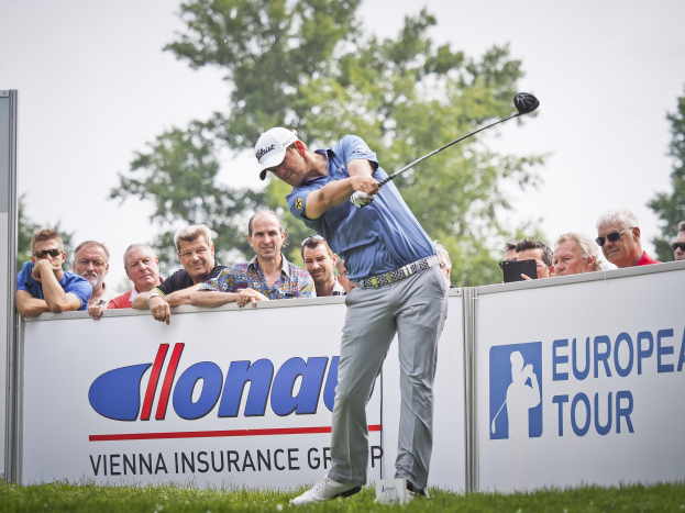 Ein Golfer mit Mücke schwingt einen Schläger auf einem grünen Feld mit Werbetafeln, Bäumen und einem blauen Himmel im Hintergrund, während der finalen Runde des European Tour.